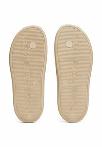 Lys beige gummisåler med teksturerede riller og cirkulære accenter; har præget "TOMMY HILFIGER" branding.