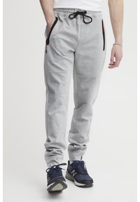 Gray sweatpants with a textured finish, black drawstring, and side zip pockets. Paired with navy athletic shoes.