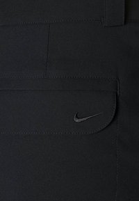 Czarne spodnie Nike mają przednią kieszeń z zaokrąglonym klapkiem oraz małym wyszywanym logo. Materiał wygląda gładko z delikatnymi detalami stębnowania.