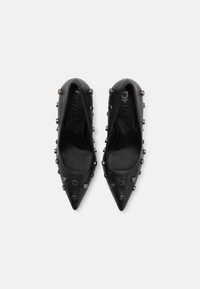 Escarpins noirs à bout pointu avec accents cloutés, présentant une surface extérieure en cuir lisse et une marque DKNY sur les semelles intérieures.