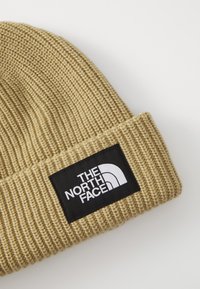 Strikket lue i lys beige med ribbet tekstur. Har en svart rektangulær lap med hvit tekst og logoen til "The North Face."