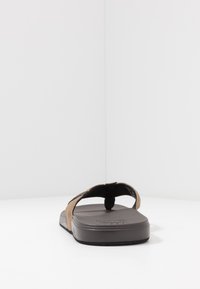 Tongs marron avec des brides texturées et une semelle en caoutchouc noir. Les brides ont une finition douce et un entre-doigt pour un bon maintien.