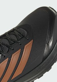 Gros plan d'une chaussure de sport noire et marron avec tissu texturé, semelle épaisse et lacets noirs à motif à pois.