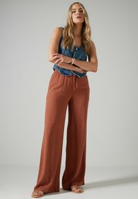 Długie, luźno dopasowane, rdzawe spodnie z elastycznym paskiem w talii, zestawione z dżinsowym topem bez rękawów. Gładka tekstura i casualowy design.