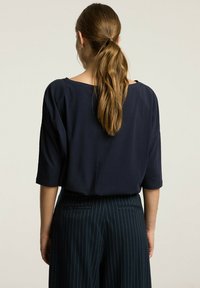 Granatowa, luźna bluzka z półrękawami, z szerokim dekoltem i miękką fakturą, w połączeniu z eleganckimi spodniami w paski.