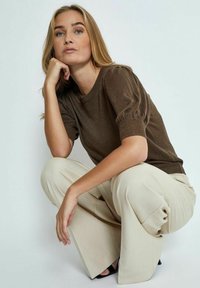 Brun metallisk stickad tröja med puffärmar, parat med krämfärgade vida byxor. Outfiten har en stilren, minimalistisk design.