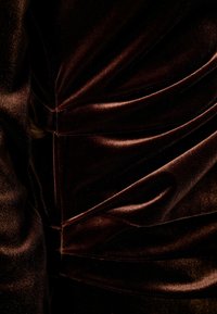 Brun sammetstyg med mjuk glans och draperad textur, med samlade sektioner och sömmar för en strukturerad design.
