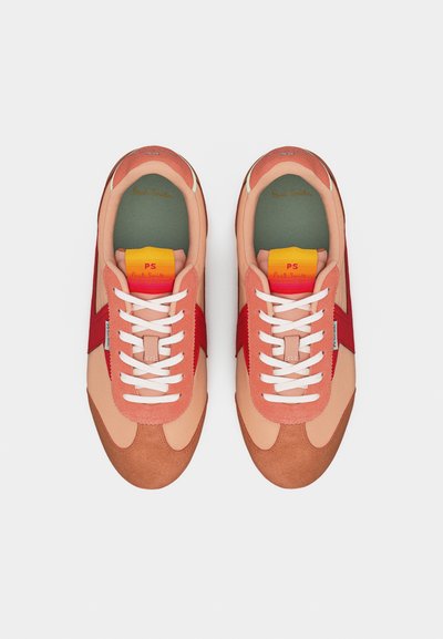 Ζευγάρι ροζ και κόκκινα αθλητικά παπούτσια με λευκά κορδόνια και ετικέτες στη γλώσσα σε κίτρινο-κόκκινο χρώμα, από πάνω σε απλό λευκό φόντο.