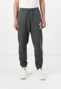 Grijze sweatpants met elastische tailleband en trekkoord, voorzien van witte gedrukte tekst aan de voorkant. Zacht stof en tapered ontwerp van de pijpen.