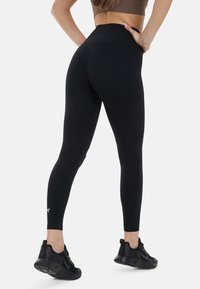 Svarta leggings med hög midja, tillverkade av stretchigt material, med en liten logotyp vid ankeln och en slät, matt yta.