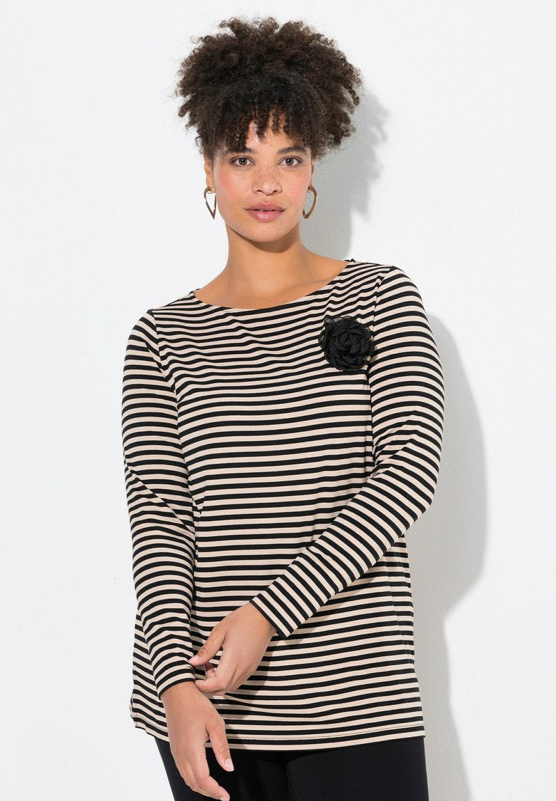 Maglia a maniche lunghe a righe nere e beige con scollo rotondo. Presenta un'accademia testurizzata nera a forma di fiore sul lato sinistro.