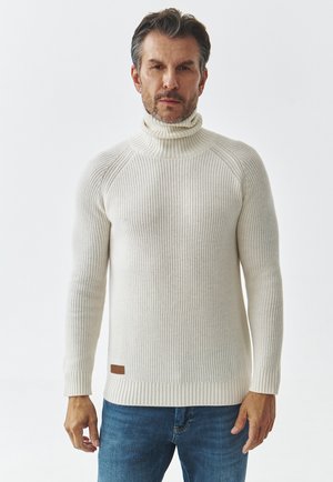 Suéter de cuello alto de punto en color blanco roto, con textura acanalada y diseño ajustado. Presenta un acento de cuero en el dobladillo y mangas largas.