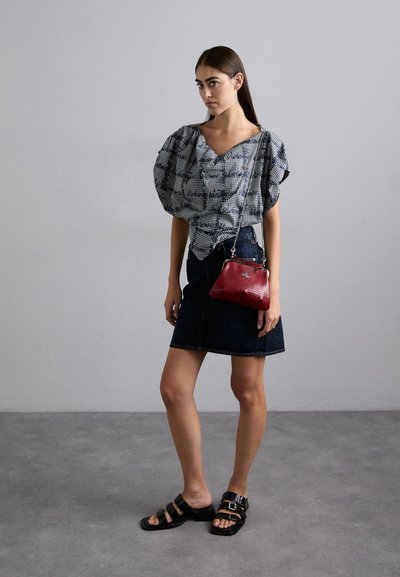 Blusa com padrão preto e branco e mangas bufantes, combinada com uma saia de ganga escura, sandálias pretas e uma pequena bolsa vermelha.