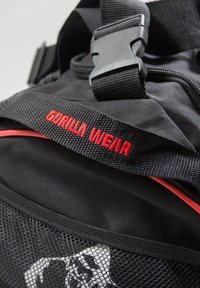 Black sports duffle bag with red accents. Features a sturdy plastic buckle and a mesh pocket with a skull pattern. "GORILLA WEAR" embroidered in red.