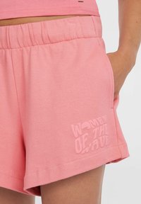 Roze katoenen shorts met een elastische tailleband, voorzien van een subtiele, getextureerde logo "WOMEN OF THE WAVE" op het linker zakgebied.