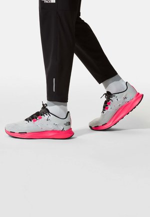 Harmaat lenkkitossut, joissa on vaaleanpunaiset yksityiskohdat, teksturoitu päällinen, mustat nauhat ja logotakilappu kantapäässä. Mustat urheiluhousut ja keskipitkät sukat.