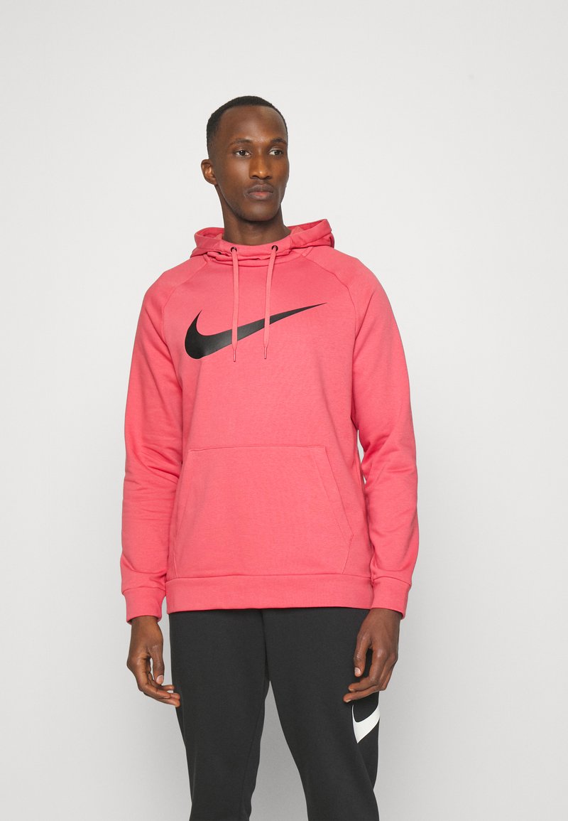 Pink hoodie with a black Nike logo, featuring a front pocket, drawstring hood, and a textured fabric, paired with dark trousers.