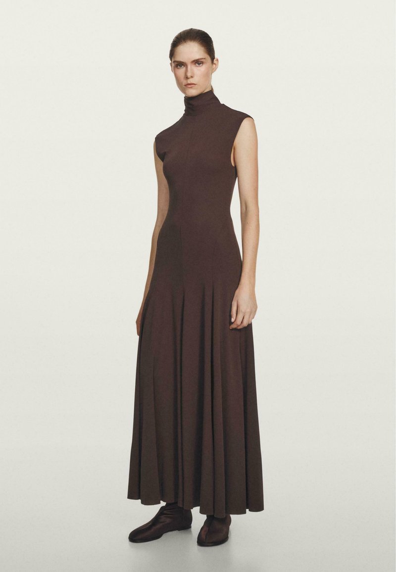 Robe marron sans manches avec un col montant, une jupe évasée et une texture lisse, associée à des bottines marron à la cheville.