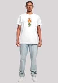 White cotton t-shirt featuring a cartoon character print in green and orange. Worn with light blue jeans and white sneakers.