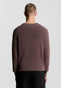 Donker mauve ribgebreide trui met een ronde halslijn, lange mouwen en een relaxte pasvorm, van de achterkant afgebeeld tegen een neutrale achtergrond.