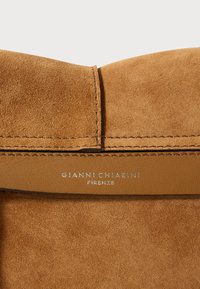 Sac en suède beige avec une bandoulière en cuir lisse, arborant une marque en relief "GIANNI CHIARINI FIRENZE," des coutures visibles et une texture douce.