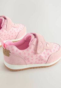 Baskets pour enfants roses avec un motif en forme de cœur, présentant une sangle en velcro, des accents en daim, un intérieur rembourré et une semelle en caoutchouc blanche.
