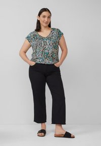 Zwarte capri-broeken met een rafelige zoom, gecombineerd met een T-shirt met korte mouwen met een kleurrijk geometrisch patroon in turquoise, wit en bruin.