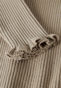 Tela de punto acanalado beig con puños con volantes, que muestra una textura suave y líneas verticales en todo el material. Vista en primer plano.