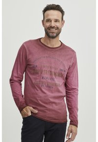 Hosszúujjú, megkopott bordó póló kerek nyakkal és sötétkék nyomtatott szövegből készült mintával. Puha tapintású, normál szabású.