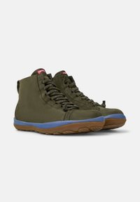 Zapatillas altas de color verde oliva con suela azul, con cordones y un pequeño logo en la lengüeta. Posicionadas sobre un fondo claro.