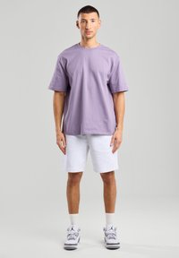 Lyhyet hihat, laventelinvärinen t-paita yhdistettynä harmaisiin shortsihousuihin, joissa on rento istuvuus ja pehmeä rakenne, käytettynä valkoisten ja harmaiden urheiluversioiden kanssa.