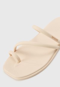 Beige flip-flop sandal made of rubber with two thin straps. Flat, square toe design with a textured footbed. Minimal branding visible.