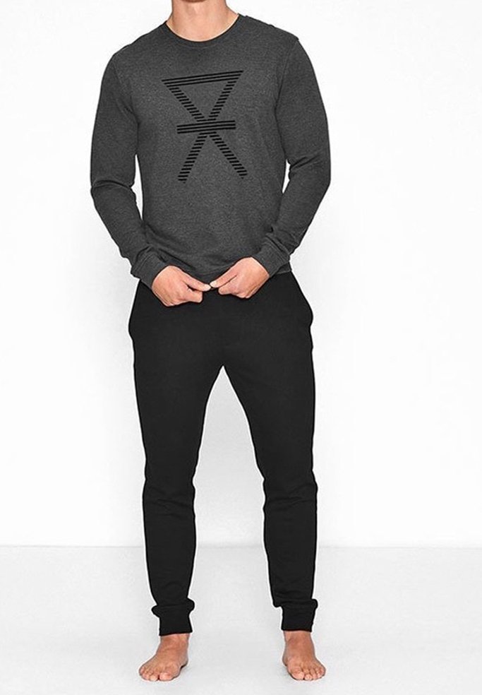 Camisa de manga larga gris con un diseño gráfico de rayas negras en la parte delantera, combinada con pantalones ajustados negros. Posición descalzo.