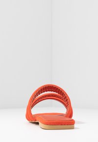 Infradito in suede arancione con due fasce larghe, suola piatta, superficie leggermente texturizzata e punta arrotondata. Design minimalista.