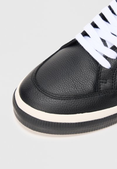 Sneaker in pelle nera con finitura testurizzata, lacci bianchi e suola in gomma color crema a contrasto. Punta rotonda e dettagli cuciti.