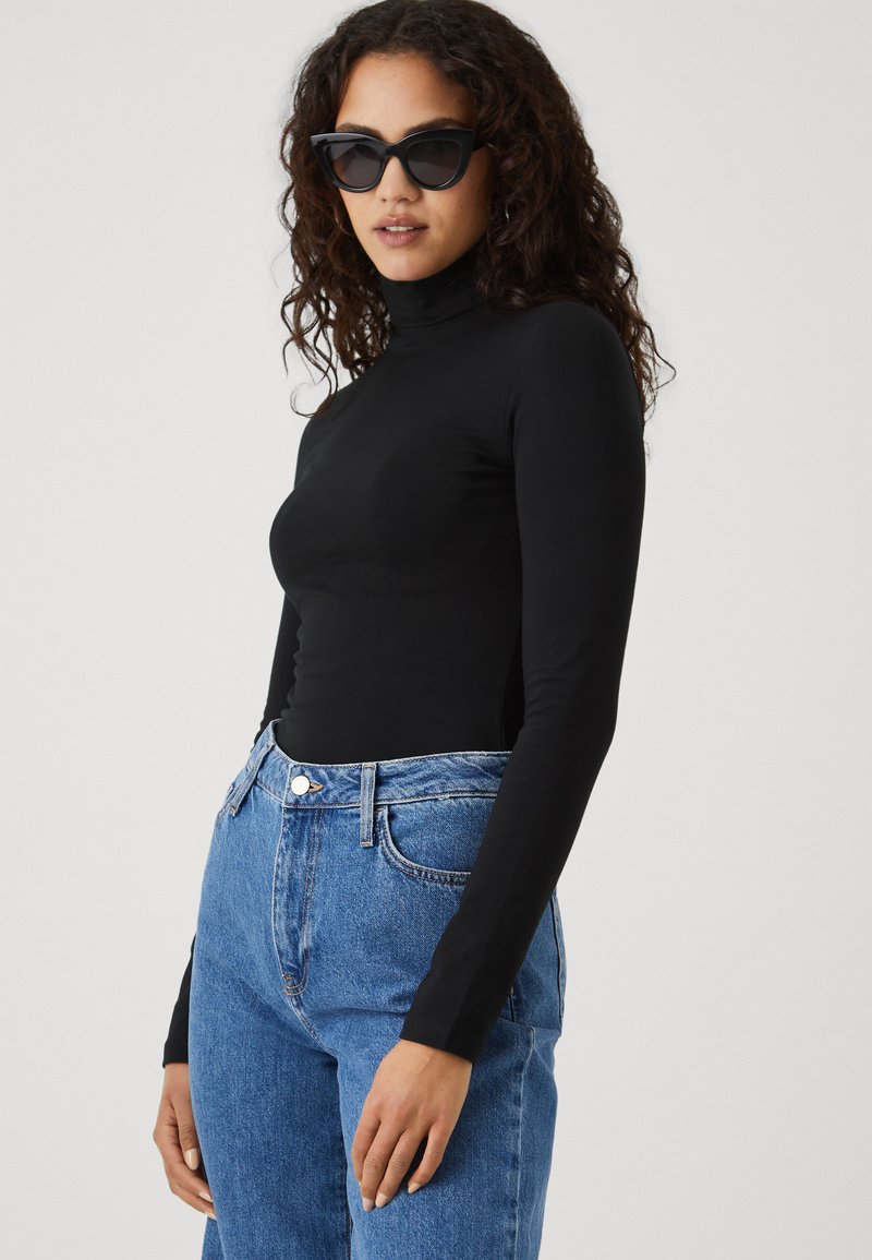 Zwarte longsleeve coltrui gecombineerd met hoog-waist lichtblauwe denim jeans. De trui is aansluitend en de jeans hebben een klassiek vijf-pocket ontwerp.