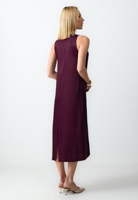 Une robe sans manches de couleur bordeaux, faite d'un tissu lisse, avec une fente sur le côté au bas et une silhouette droite.