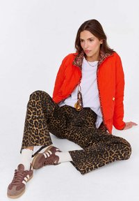 Pomarańczowa pikowana kurtka z podszewką w leoparda, biały t-shirt, brązowe spodnie w leoparda oraz brązowe trampki z białymi paskami.