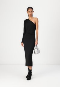 Svart, off-shoulder kjole med lang erme, gulvlengde design. Kombinert med en liten sølvveske og svarte sko med stropper. Glatt tekstur.