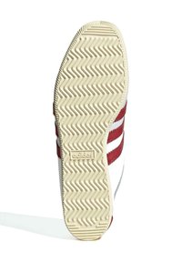 Adidas skosula med en krämfärgad strukturerad gummibotten, som har ett zigzagmönster och röda accentränder på sidan.