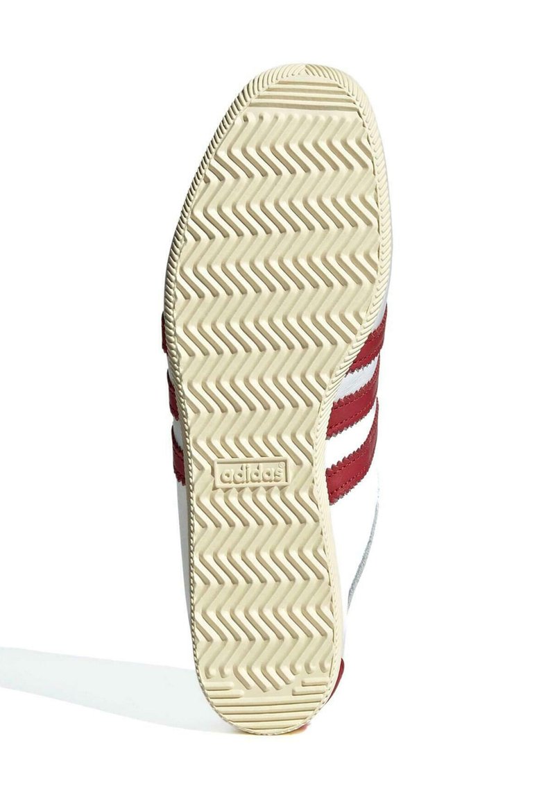 Adidas-Schuhsohle mit einem cremefarbenen, strukturierten Gummiboden, der ein Zickzackmuster aufweist und rote Akzentstreifen an der Seite hat.