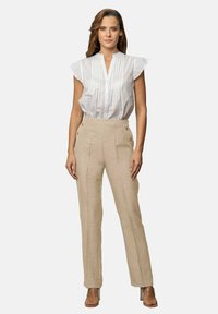 Blusa blanca de manga corta con un patrón texturizado y pliegues verticales, combinada con pantalones de lino beige de tiro alto con botones laterales.