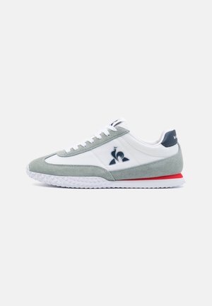 Baskets en cuir suédé vert clair et en cuir blanc avec une semelle en caoutchouc, présentant un logo sur le côté et un accent rouge au niveau du talon.