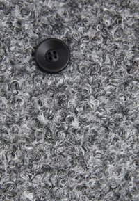 Textured gray fabric with prominent curly fibers and a black two-hole button. The material appears soft and fuzzy, showcasing a layered look.