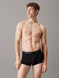 Fekete pamut boxer alsónadrág testhezálló fazonnal és elasztikus derékszíjjal, amelyen fehér "Calvin Klein" logó található. A modell profilból látható.