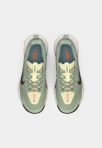 Sapatilhas de corrida de trilha Nike de verde claro com parte superior em malha, detalhes em preto e logótipo em laranja brilhante, apresentando uma sola texturizada e língua acolchoada.