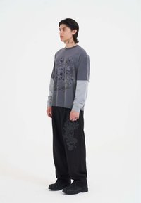 Gray long-sleeve shirt with dark graphic print, paired with black pants featuring a dragon design and chunky black footwear.