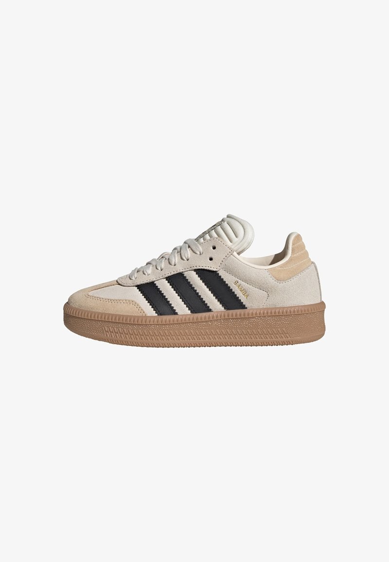 Beige suede sneakers with three black stripes, white accents, and a rubber gum sole. Features a soft padded tongue and textured detailing.