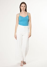 Lichtblauw hemdtopje met kanten rand, gecombineerd met hoge witte wijde broek met een riem. Sleehak sandalen in het wit maken de look af.