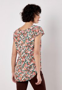Blusa floreale in tessuto di cotone con sfondo verde, fiori rosa e bianchi, maniche corte e dettaglio a chiave sulla schiena.
